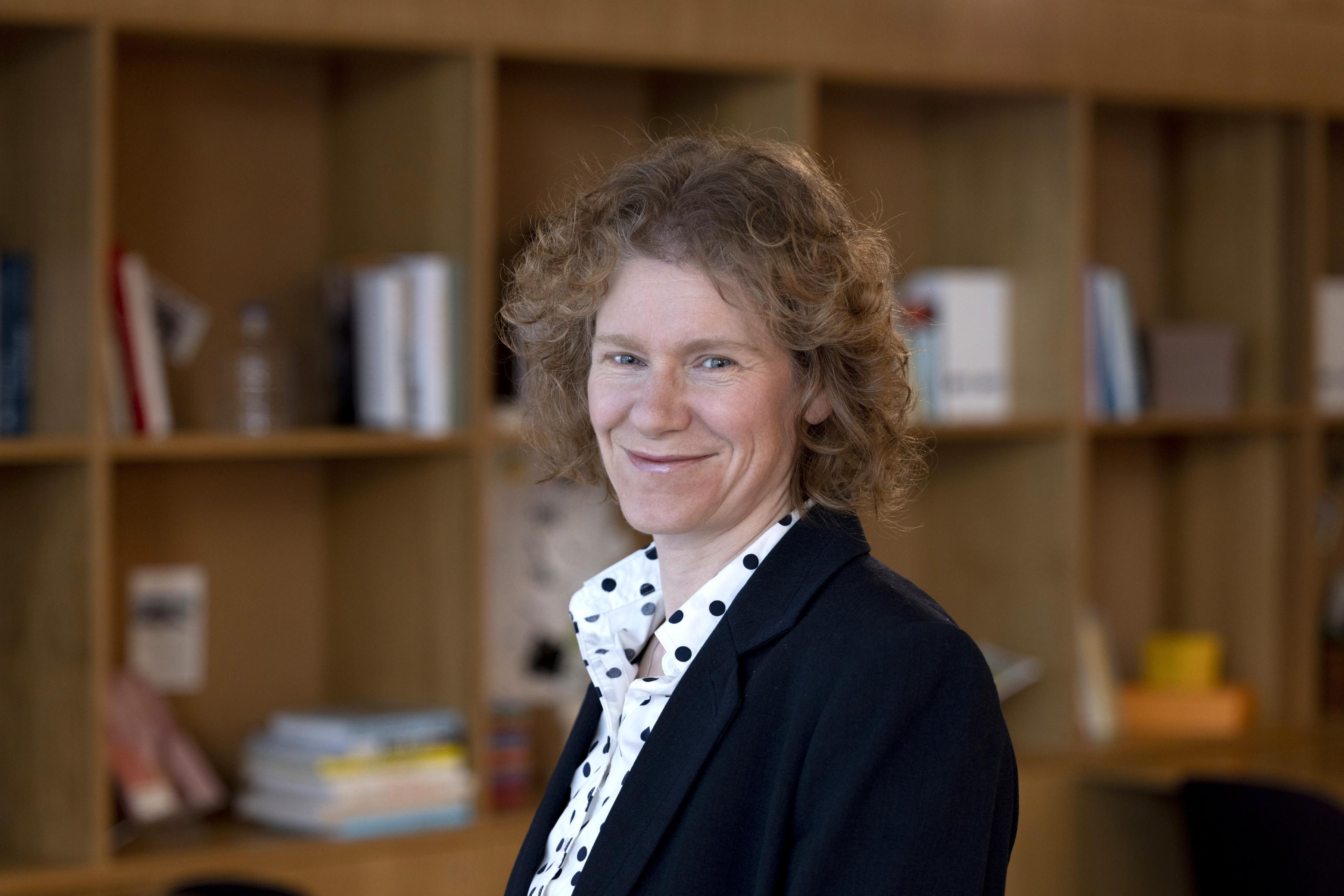 Fiona Schaefer, Innovation Manager, standing in front of a bookcase and smiling towards the camera. She is wearing a black suit jacket, with black and white polka dot shirt.